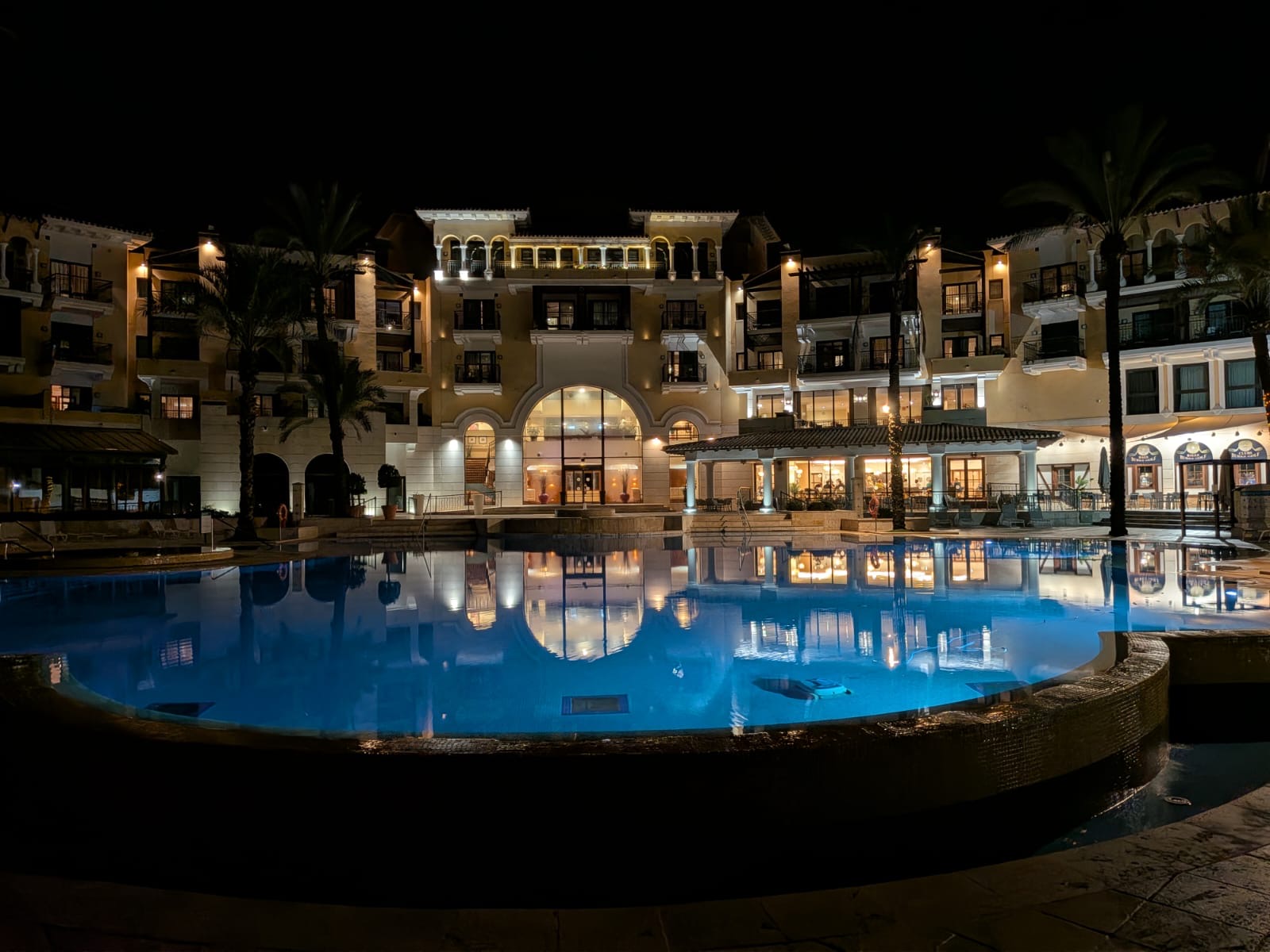 Beleuchtete Fassade des 5-Sterne-Resorts spiegelt sich nachts im Pool